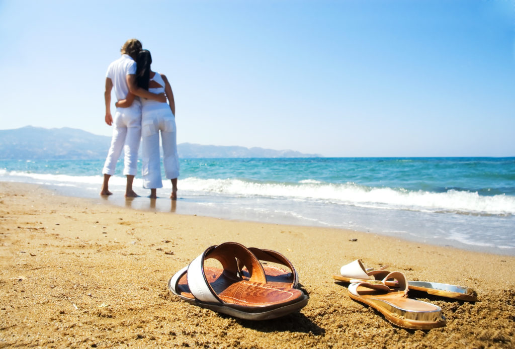A pair of sandals on the beach with two people in the background.