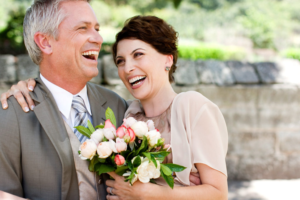 A man and woman smiling while holding flowers.