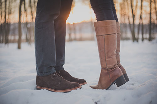 Two people standing in the snow wearing boots.