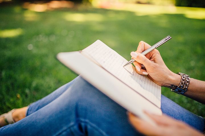 A person writing in a notebook on the grass.