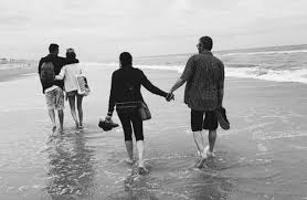 A man and woman holding hands while walking on the beach.