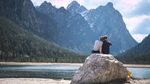 Two people sitting on a rock near the water.