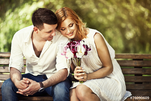 A man and woman sitting on a bench holding flowers.