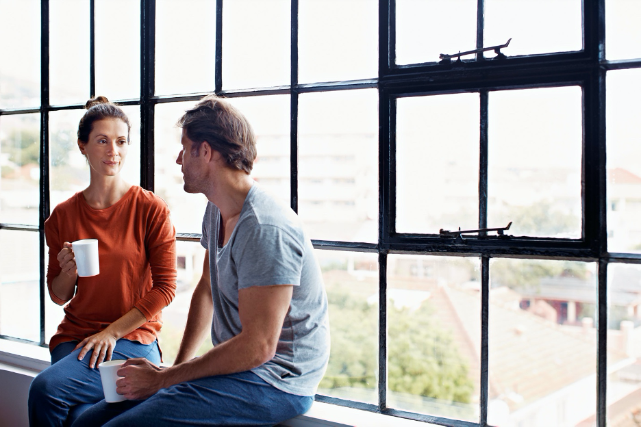 A man and woman sitting on the ground in front of a window.
