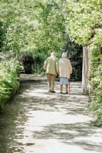 Two older people walking down a path in the woods.